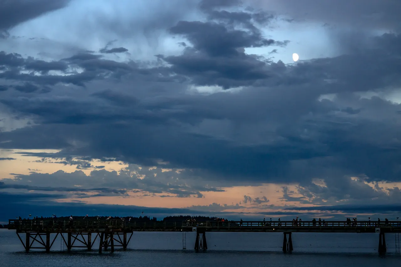 Moon Rising Over Silhouetted Pier Under Dramatic Storm Clouds at Dusk
