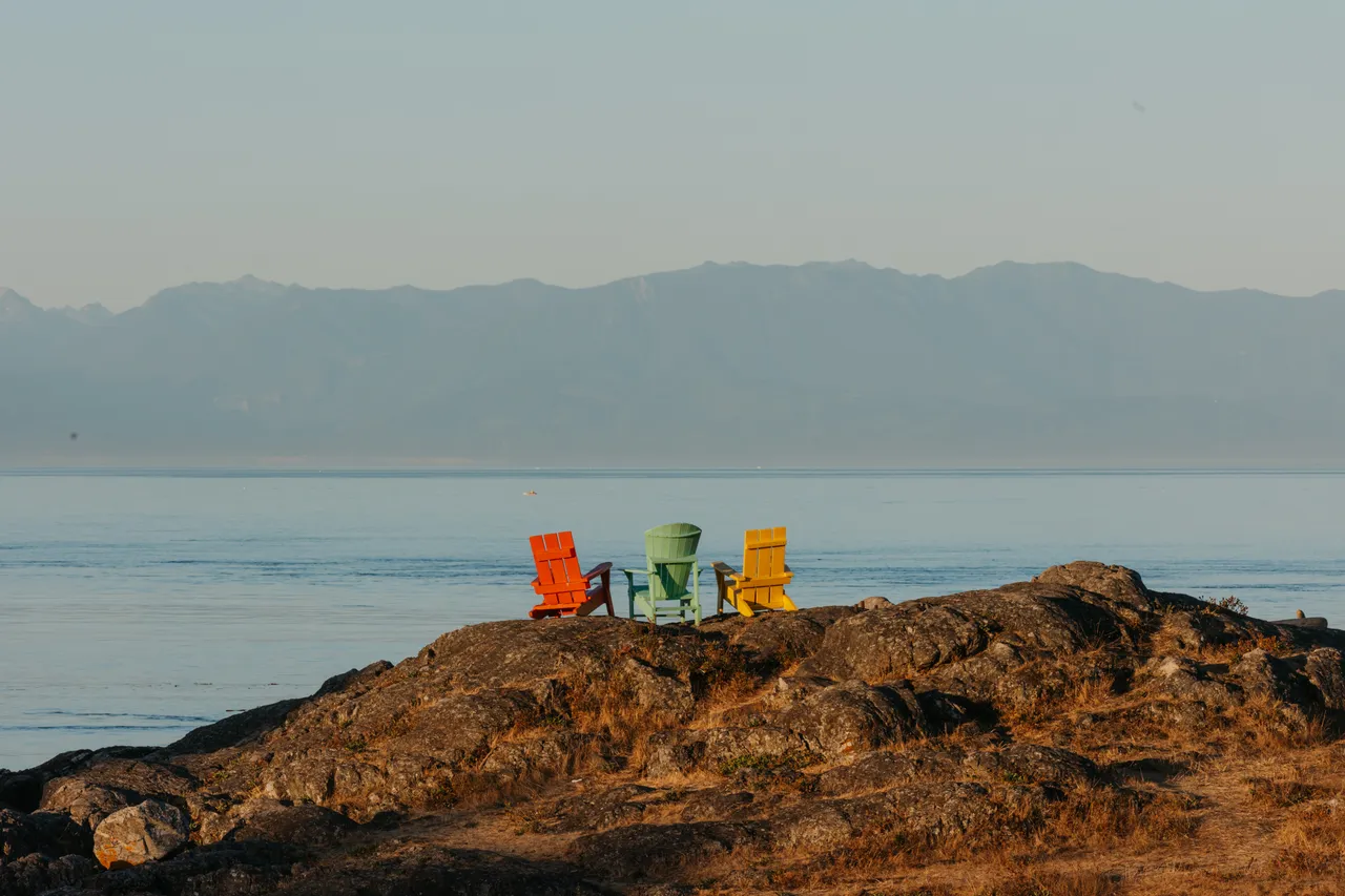 Colourful chairs overlook calm ocean and distant mountains
