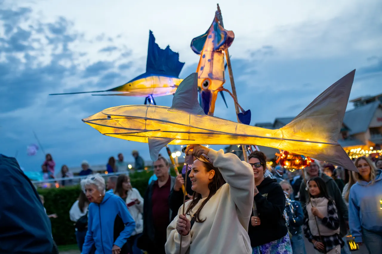 Giant shark and swordfish lanterns held above a smiling crowd at blue hour