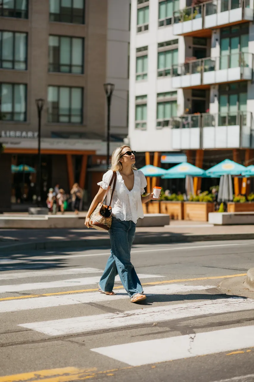 Woman Crossing Street with Apartment Buildings in Background on Sunny Day